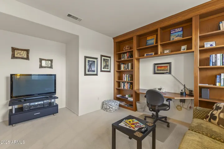 Spacious den with built-in shelving, TV area, and a comfortable seating nook—ideal for productivity or relaxation in this energy-efficient Surprise home.