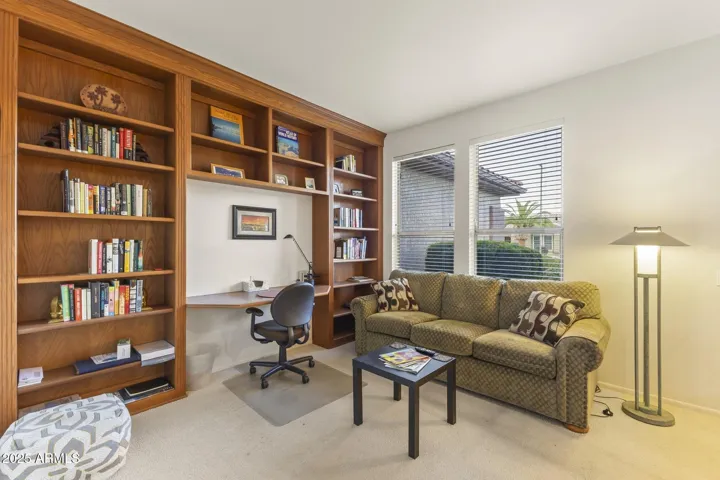 Beautiful custom wood shelving with integrated desk creates a warm, functional workspace ideal for remote work or creative projects. Large windows fill the room with natural light.