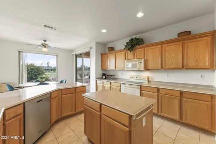 Beautiful kitchen with center island, wood cabinetry, and scenic golf course views through large picture windows. The open layout offers a warm, inviting space for cooking and entertaining.