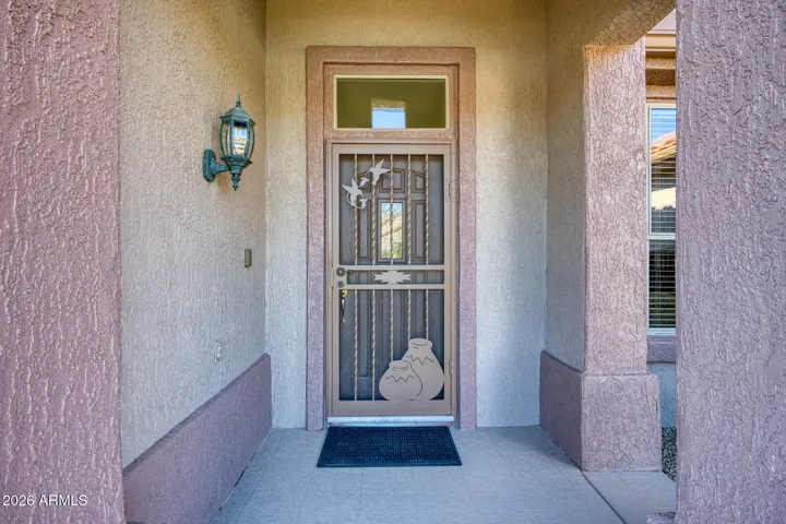 Covered front porch with custom iron door and decorative lighting, showcasing pride of ownership and timeless desert architecture.