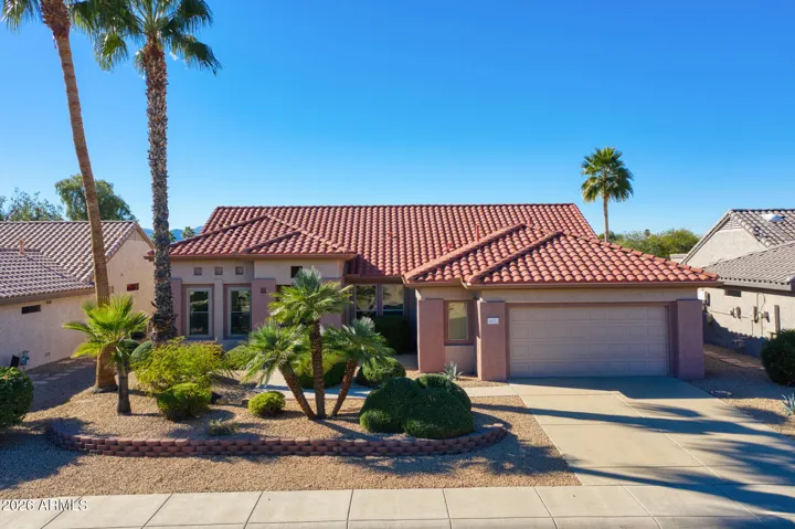Stunning front view of this Surprise, AZ golf course home with red tile roof, lush palms, and desert landscaping. Enjoy serene mountain views and perfect curb appeal in this energy-efficient residence.