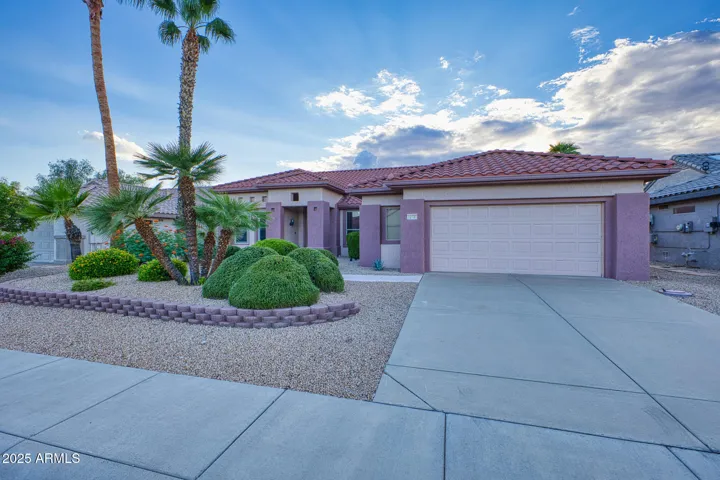 Vibrant front yard featuring palm trees, blooming lantana, and a tiered stone border that highlights the home’s Arizona-style architecture.