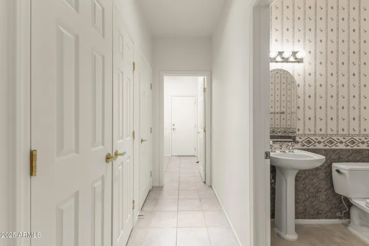 Clean, light-filled hallway featuring neutral tile flooring, white doors, and access to guest rooms and bath, offering a seamless flow through the home.
