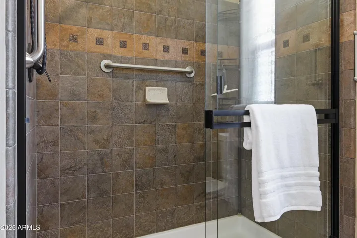 Custom tiled walk-in shower includes grab bars and easy to close glass shower doors!