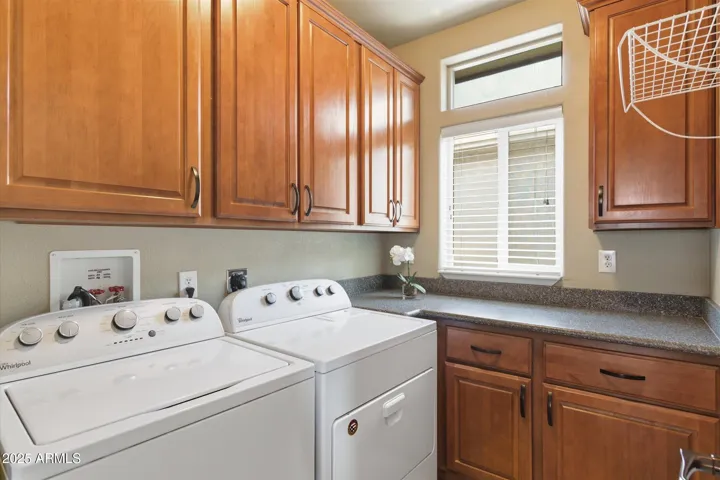 The home includes the washer and dryer with lots of cabinet's with a folder table and windows with blinds.