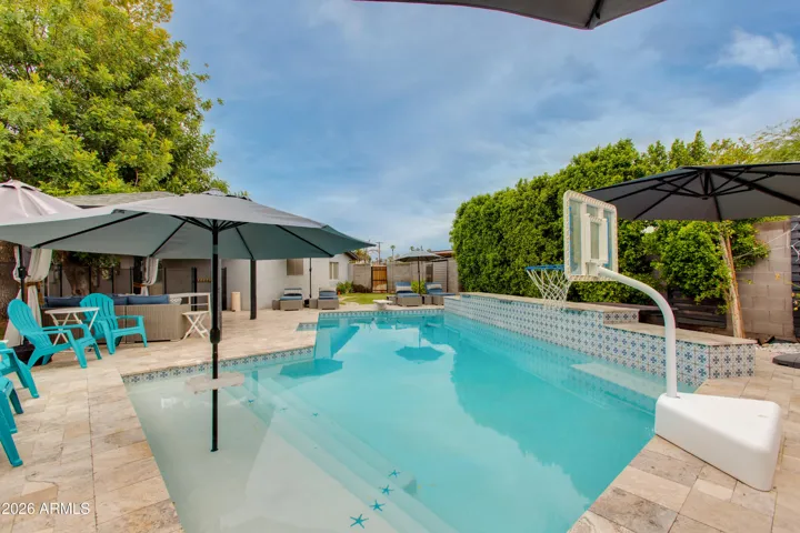 Resort-style backyard oasis with a sparkling pool, travertine pavers, and eye-catching patterned tile. Built-in umbrella sleeves in the shallow tanning area offer perfect shade, while the raised pool wall adds style and extra seating. Multiple lounge spaces, pergola & lush privacy hedges make this the ultimate space for relaxing or entertaining year-round in Arizona.