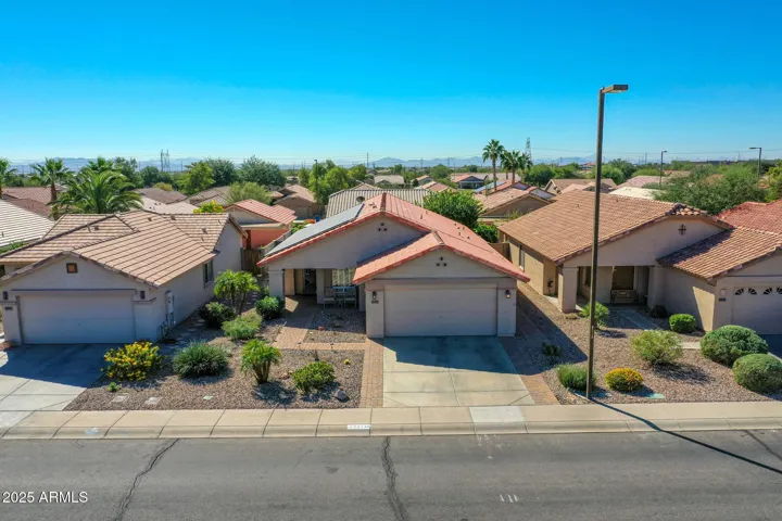 A closer aerial view highlights the home’s roofline and installed solar panels, emphasizing energy efficiency and long-term savings. The image captures the home’s position along the street with neighboring residences, desert landscaping, and well-kept sidewalks, reinforcing the appeal of this Buckeye property for buyers focused on sustainability.