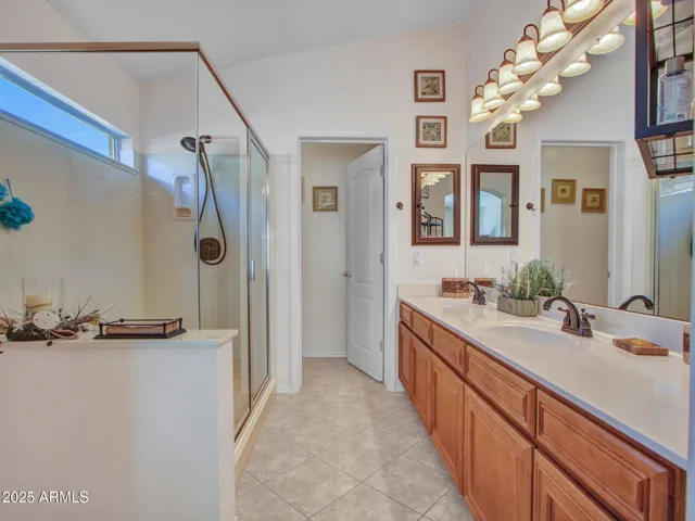 Primary bathroom offers a double-sink vanity, expansive countertop space, warm cabinetry, and tile flooring for both style and functionality.