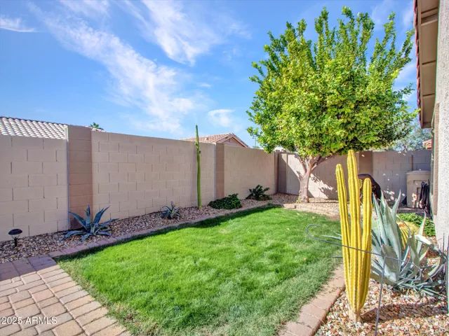 Rear exterior view highlighting the covered patio, paver entertaining areas, and landscaped yard for year-round enjoyment.