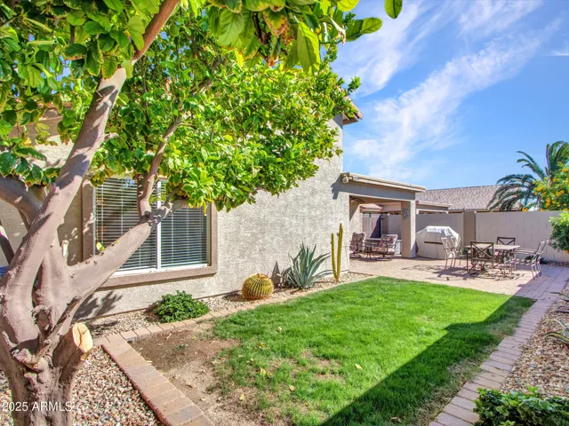 Wide backyard view showcasing covered patio, paver entertaining area, and grassy lawn, offering versatile outdoor space.