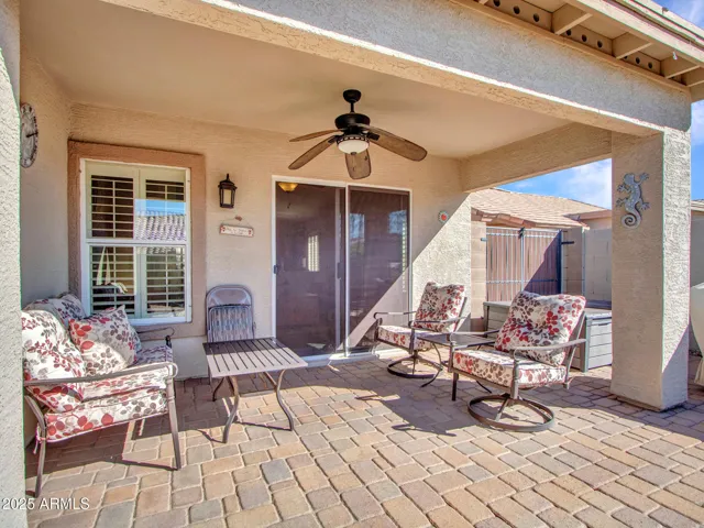 Inviting covered patio with comfortable seating and paver flooring, offering a private outdoor retreat with easy access to the home.