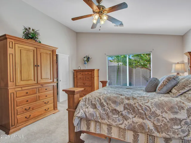 Primary bedroom showcasing generous space, ceiling fan, carpet flooring, and room for full-size furnishings and storage.