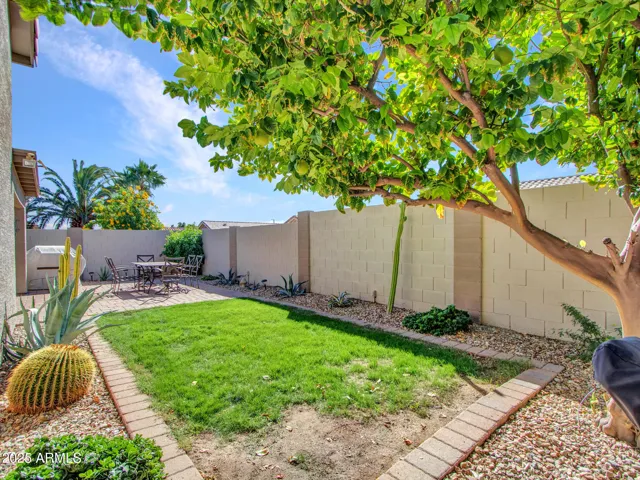 Backyard features a green lawn bordered by desert landscaping and paver edging, blending beauty with easy upkeep.