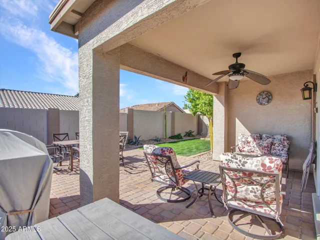 Spacious covered patio overlooking the landscaped backyard, featuring pavers, ceiling fan, and room for outdoor gatherings.