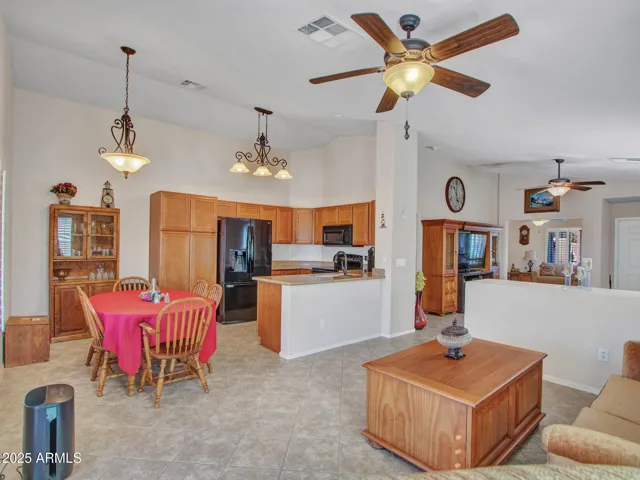 Wide-angle view of the family room flowing into the dining area and kitchen. Tile flooring and ceiling fans enhance comfort and energy efficiency.