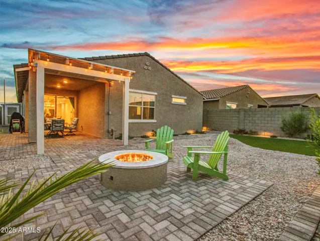 This beautifully finished Litchfield Park backyard showcases a paved patio, fire pit, pergola, and low-maintenance landscaping, perfect for outdoor entertaining. The space highlights energy-efficient living with artificial turf and a stunning sunset backdrop.