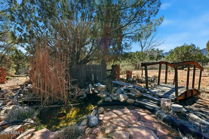 Charming koi pond with stone edging and wooden bridge surrounded by mature trees creating a peaceful garden retreat in Hackberry AZ.
