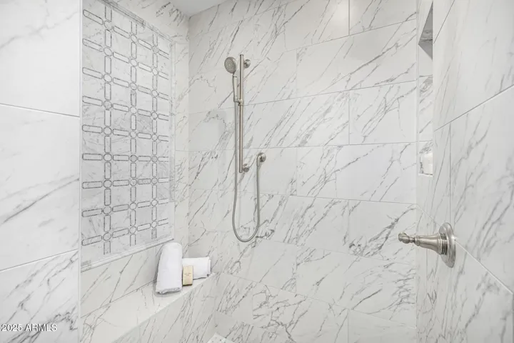 The elegant and functional walk-in shower features a bench seat, shampoo niche, and tasteful tile inset design.