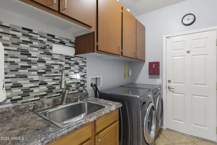 Inside laundry room w upgraded, front loader washer/dryer, utility sink w vanity, plenty of cabinets, deco backsplash