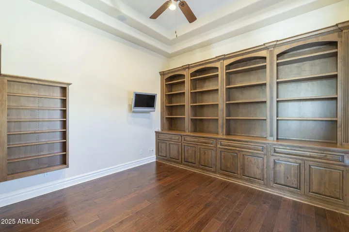 Beautiful den featuring hardwood floors, ceiling fan, TV on articulated mount and built in shelving and storage with view to courtyard.