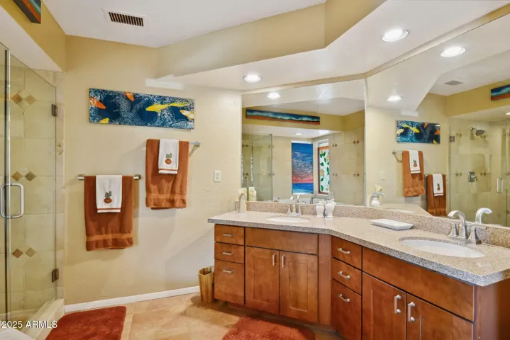 A well-appointed primary bathroom features a double sink and spacious wooden cabinetry to store all essential toiletries. A large mirror and a modern walk-in shower add both style and convenience. The roomy jetted bathtub invites you to lie back and relax after a long day.