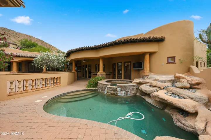 Resort-style backyard featuring a rock-accented pool, integrated heated spa, and covered patio