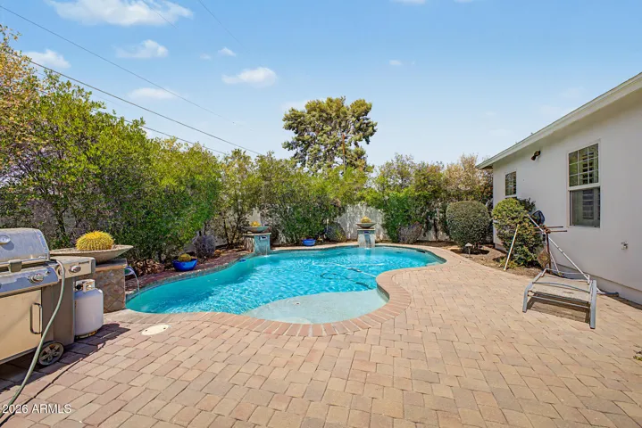 Expansive backyard showcasing a resort-style pool, mature greenery, and paved patio areas. This Phoenix home offers seamless indoor-outdoor living with plenty of space to unwind.