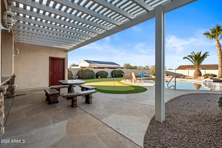 Shaded pergola seating area featuring decorative concrete table and benches that convey with the property. Positioned near the pool and putting green, offering a relaxing spot for dining, conversation, or evening enjoyment.