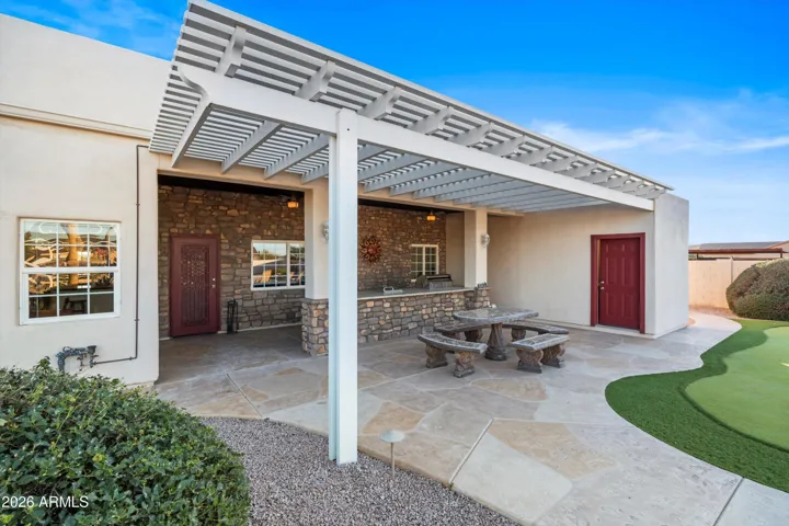 Rear patio view showcasing the covered outdoor kitchen, concrete seating area, and convenient poolside bathroom with sink and toilet. Designed for seamless outdoor living, entertaining, and everyday use.