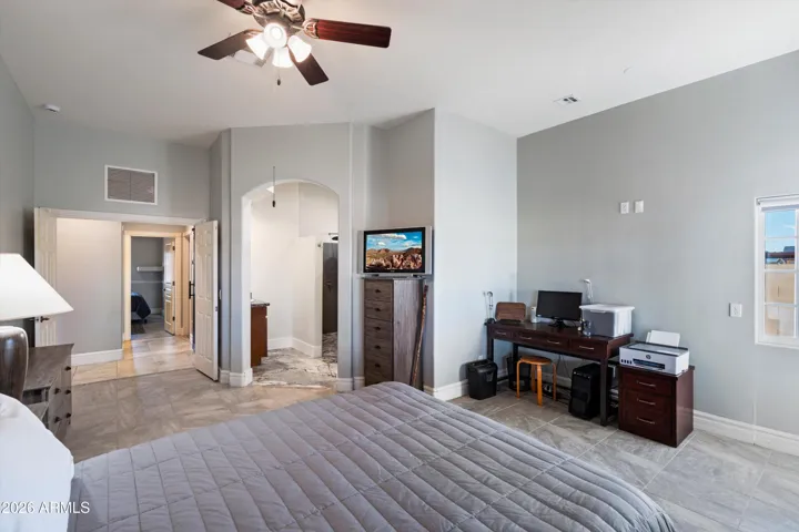 The primary bedroom provides a generous layout with tile flooring, neutral tones, and room for a sitting area or workspace. An ensuite bathroom and walk-in closet complete the suite, creating a private retreat within the home.
