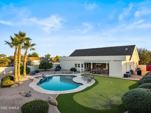 Aerial perspective highlighting the full backyard layout, including pool, spa, putting green, covered patio, and the scale of the home and outdoor living areas.