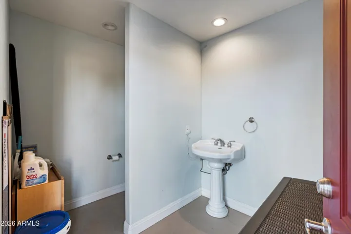Convenient poolside bathroom with toilet and pedestal sink, allowing guests easy access without entering the main home. A thoughtful addition for outdoor gatherings and everyday pool use.