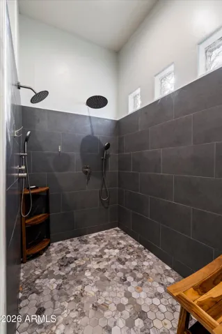 The walk-in shower has been fully renovated with modern tile, multiple shower heads, and glass block windows that bring in natural light while maintaining privacy. A bench and open layout add both comfort and style.