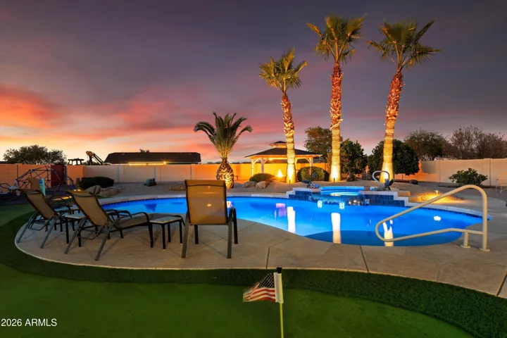 The backyard showcases a heated and cooled pool with a self-cleaning system and spillover spa. Surrounded by hardscape, seating areas, and landscape lighting, this outdoor space is designed for entertaining and everyday enjoyment.