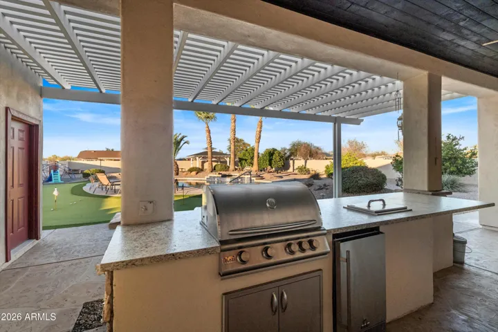 Outdoor kitchen area under a covered patio with built-in BBQ, prep counters, refrigerator, and ice chest. Ideal for hosting, casual meals, and enjoying Arizona evenings with seamless access to the pool and yard.