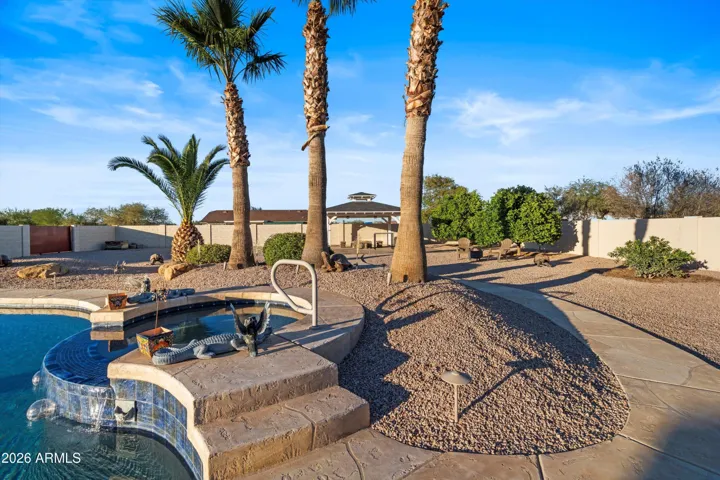 Heated and cooled spa with cascading water feature flowing directly into the pool. Surrounded by mature palms, stone and stamped concrete decking for a resort-style experience.