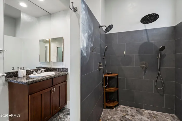 The primary bathroom features a modern walk-in shower with dual shower heads, sleek tile finishes, and a granite-topped vanity. Designed for both function and relaxation, this space offers a clean, contemporary feel.