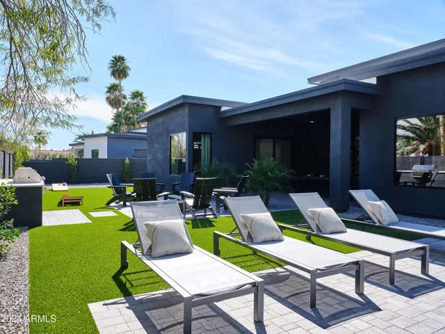 Resort-like backyard with a covered patio offering outdoor dining, a sparkling blue heated pool with sun loungers, yard games, a BBQ grill and a fire pit.