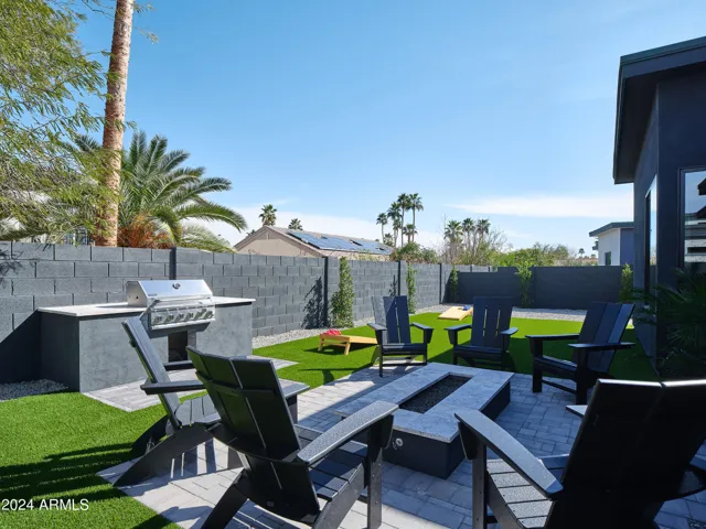 Resort-like backyard with a covered patio offering outdoor dining, a sparkling blue heated pool with sun loungers, yard games, a BBQ grill and a fire pit.