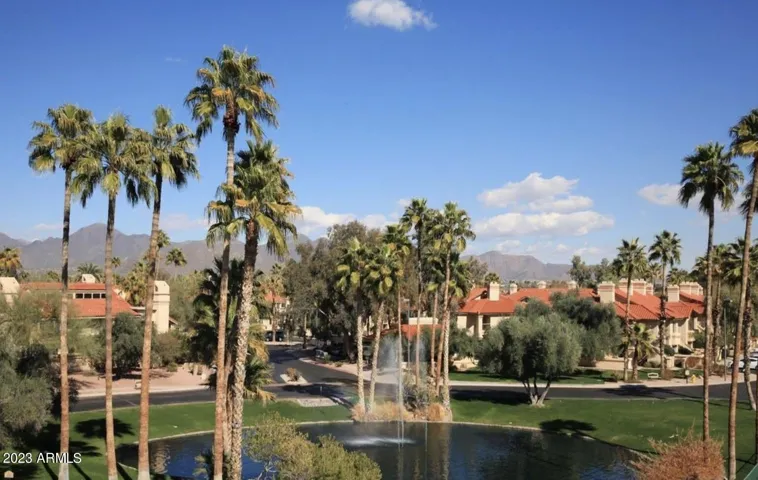 Peaceful lake with fountain framed by palm trees and distant mountain views, offering a tranquil retreat within this Scottsdale gated community. Lush landscaping and walking paths enhance the resort-style setting.