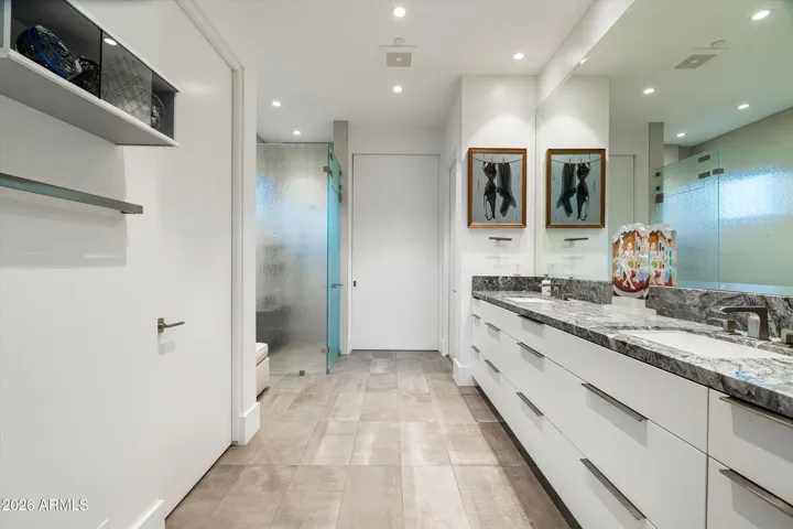 The primary bath showcases dual water closets, a walk-in closet with floor-to-ceiling storage and a central island, a double vanity, and pocket doors that provide added privacy between the bedroom and closet.