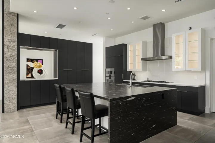 Oversized kitchen island showcasing waterfall-edge leathered granite countertops with abundant storage on both sides, blending striking design with everyday functionality.