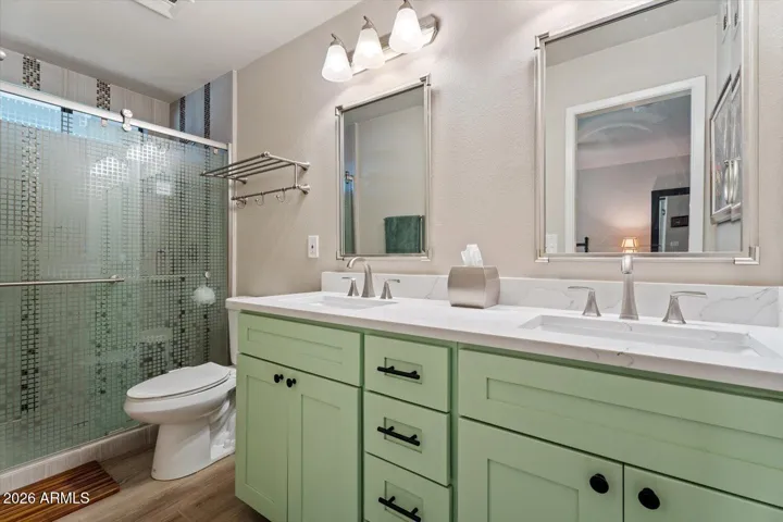 Tastefully renovated primary bathroom with dual vanities, cabinetry for storage and a glass door shower.