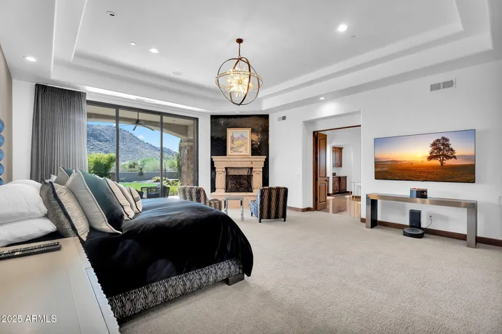 Primary bedroom with sitting area, cantera stone fireplace, and breathtaking Troon and backyard vistas, plus visible entrance to the primary bath.