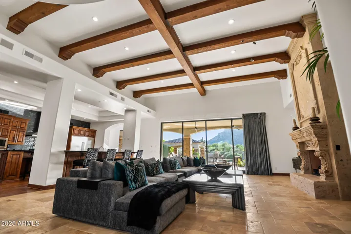 Spacious and inviting great room with towering 20' ceilings, warm wood beams, cantera fireplace, and sliding glass doors opening to outdoor living