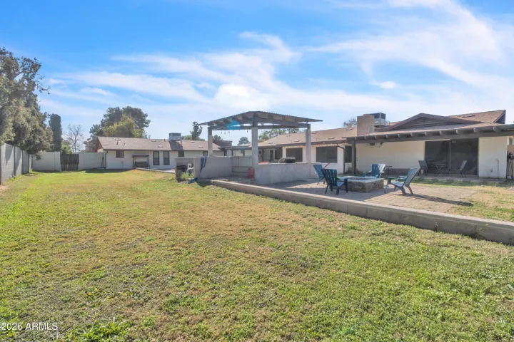 A backyard built for gathering — firepit conversations, shaded ramada seating, BBQs, real grass, and poolside Arizona living.