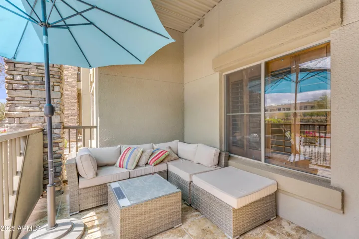 Enjoy indoor-outdoor living on this covered patio featuring comfortable seating and stone accents. This inviting outdoor space offers privacy and a relaxing setting ideal for morning coffee or evening downtime in a well-maintained Phoenix community.