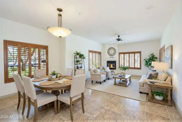 This beautifully appointed living room features a cozy gas fireplace, large windows with plantation shutters, and an open layout that flows effortlessly into the dining space. With neutral tones and natural light, this space perfectly blends comfort and style, ideal for relaxing or entertaining in your Phoenix home.