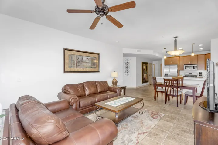 The airy living room features large windows with plantation shutters that frame peaceful community views. An open layout and ceiling fan provide a comfortable space ideal for relaxing or entertaining.