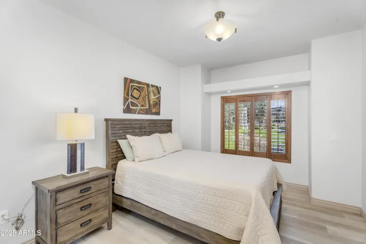 The second bedroom offers privacy and comfort with a serene greenbelt view, modern light fixture, and wood-style flooring—ideal for guests, a roommate, or home office needs.